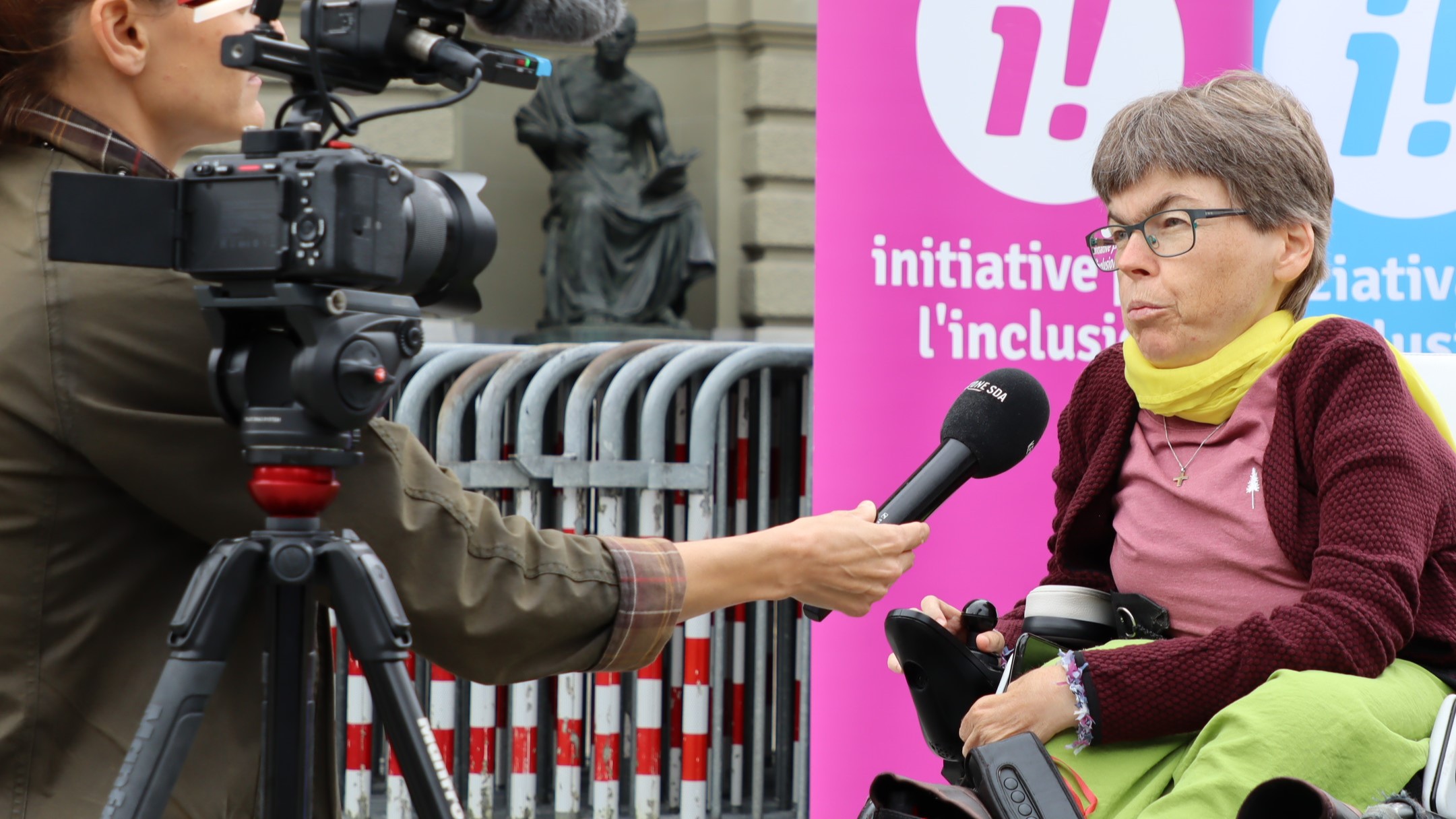 Simone Leuenberger bei einem Interview mit einer Journalistin mit Kamera und Mikrophon. Im Hintergrund Banner der Inklusions-Initiative und das Bundeshaus.